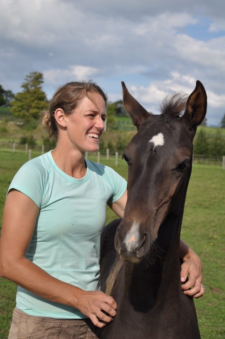 A woman smiling with a dark bay Akhal-Teke foal