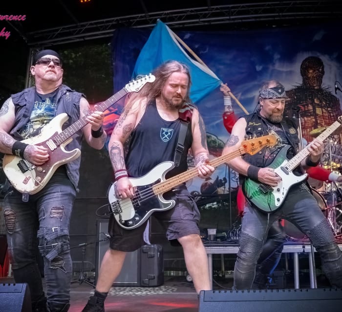 Ey Up Maiden live at Saltaire Festival 2026: Tony Rushworth (lead guitar), Nic Sheen (guitar) and Kurt 'Bomber' Evans (bass) with the Yorkshire flag