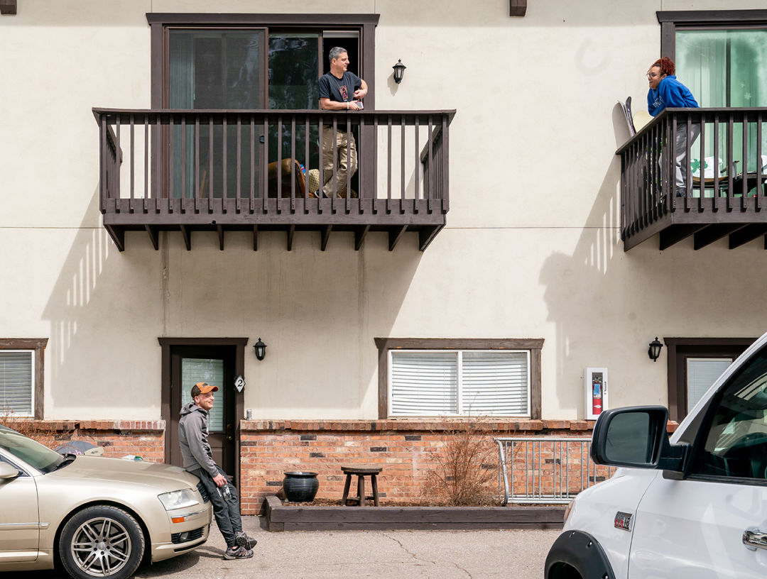 Two people chat from their apartment balconies while a third stands on the ground below them