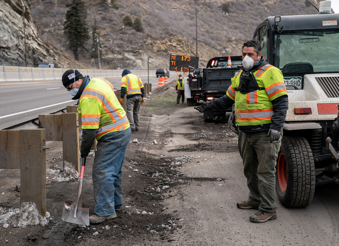 Workers wearing protective masks clear a roadside trail