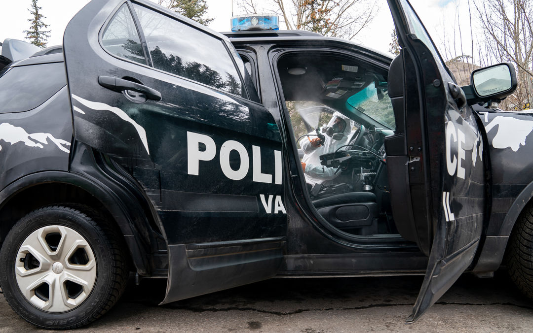 A person wearing white protective gear sprays the interior of a police car