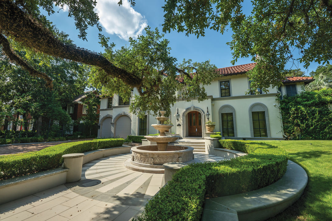 A white mansion with a corrugated roof with a fountain out front.