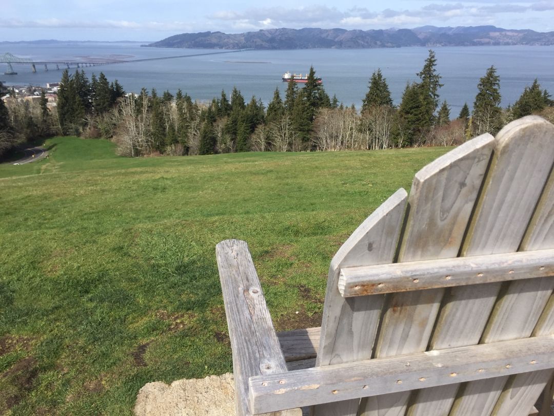 The back of a wooden Adirondack chair and a view of a sloping hill and the Columbia River