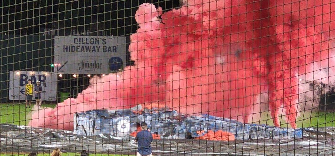 A model of a beached whale behind second base on a baseball field, with pink smoke streaming from it and pick stuff oozing out at the bottom