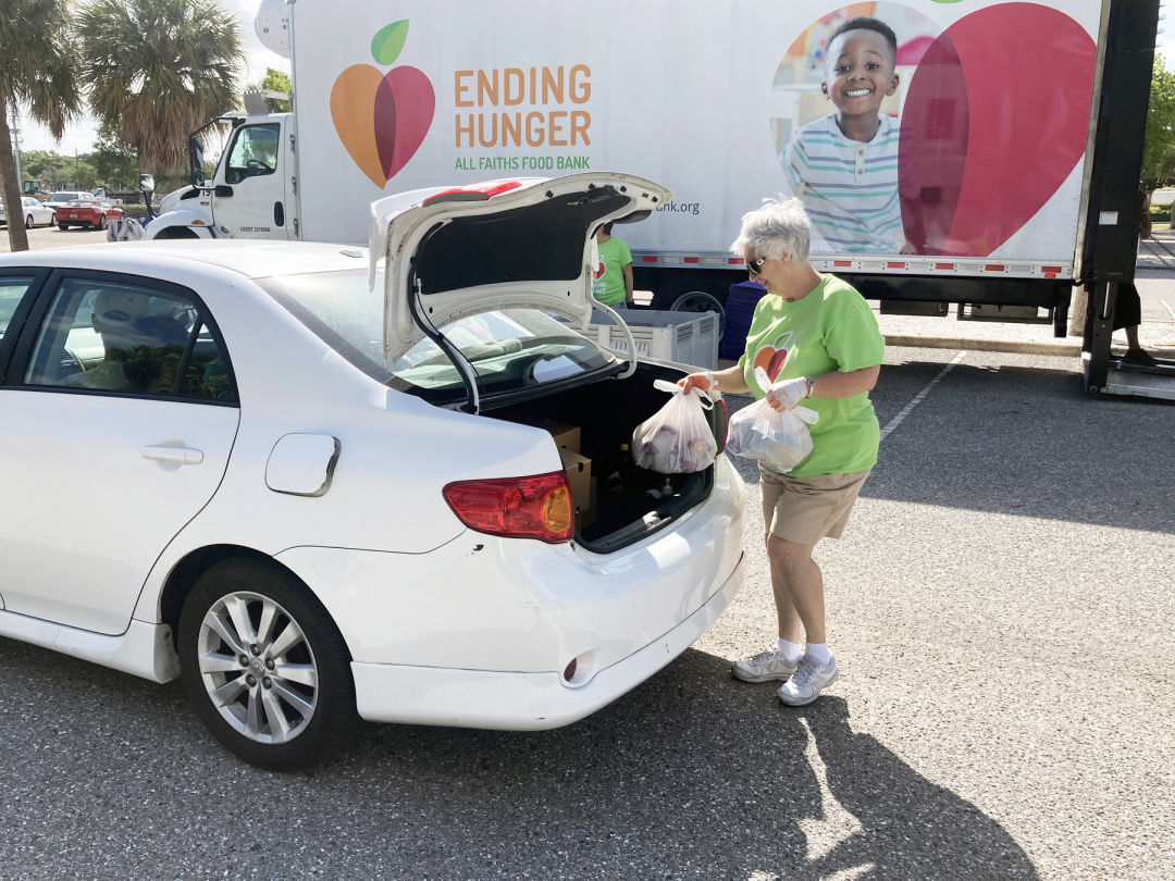 All Faiths Food Bank volunteer Maureen Donahue helps to load food into a community member's car during the May food distribution at Van Wezel