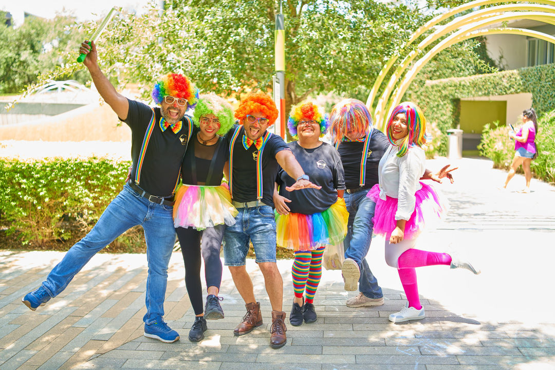 A group of people dressed in rainbow clown outfits smiling and posing.
