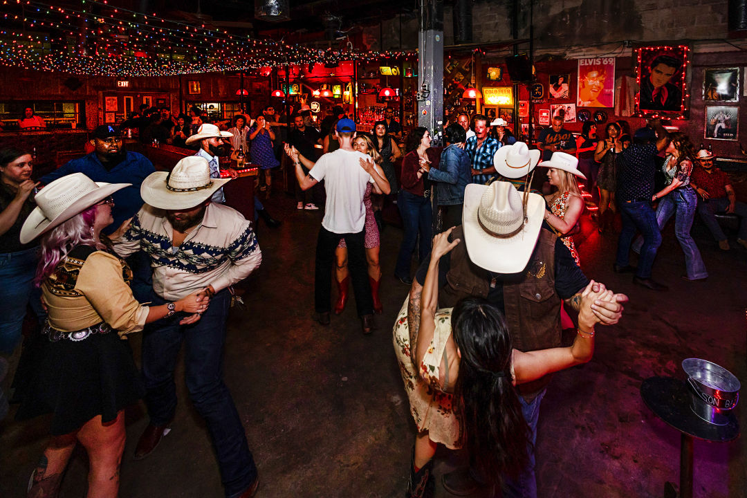 A group of people in western wear dancing at a bar.