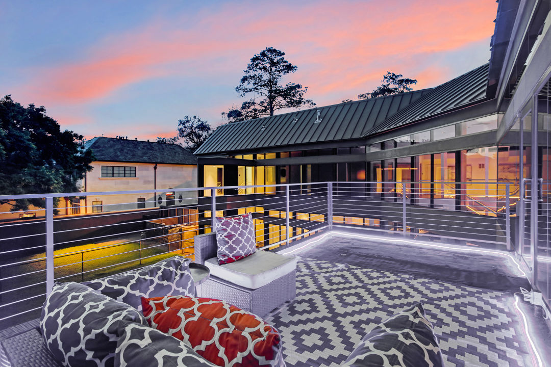 A furnished balcony behind a large postmodern house.