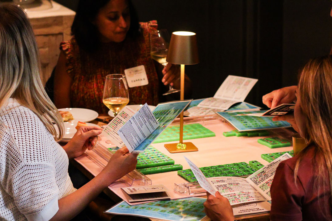 Green mahjong tiles are arranged on a table, surrounded by four women