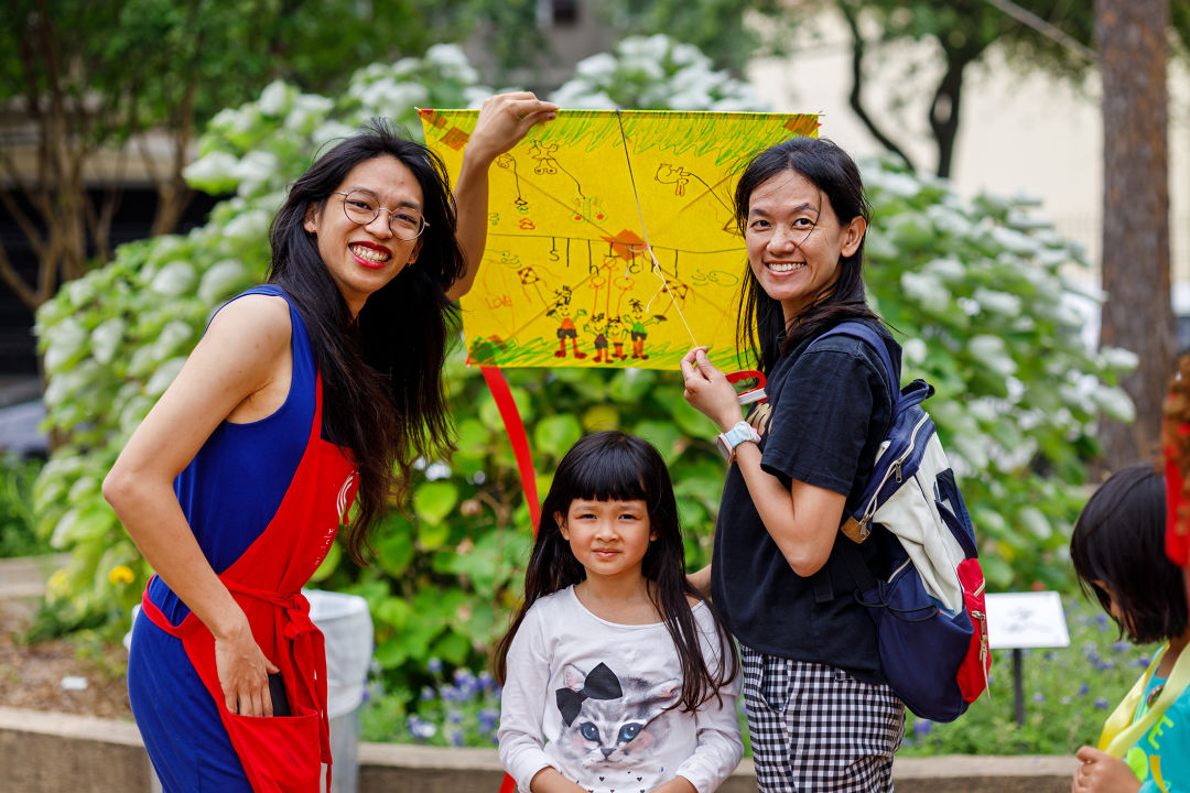 Three people and posing with a handmade yellow kit. The two adults are smiling and a small child is frowning.