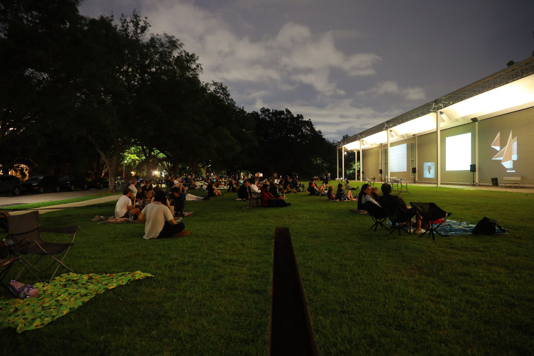 People on the lawn of the Menil Collection in Houston, watching films projected onto the side of the building.