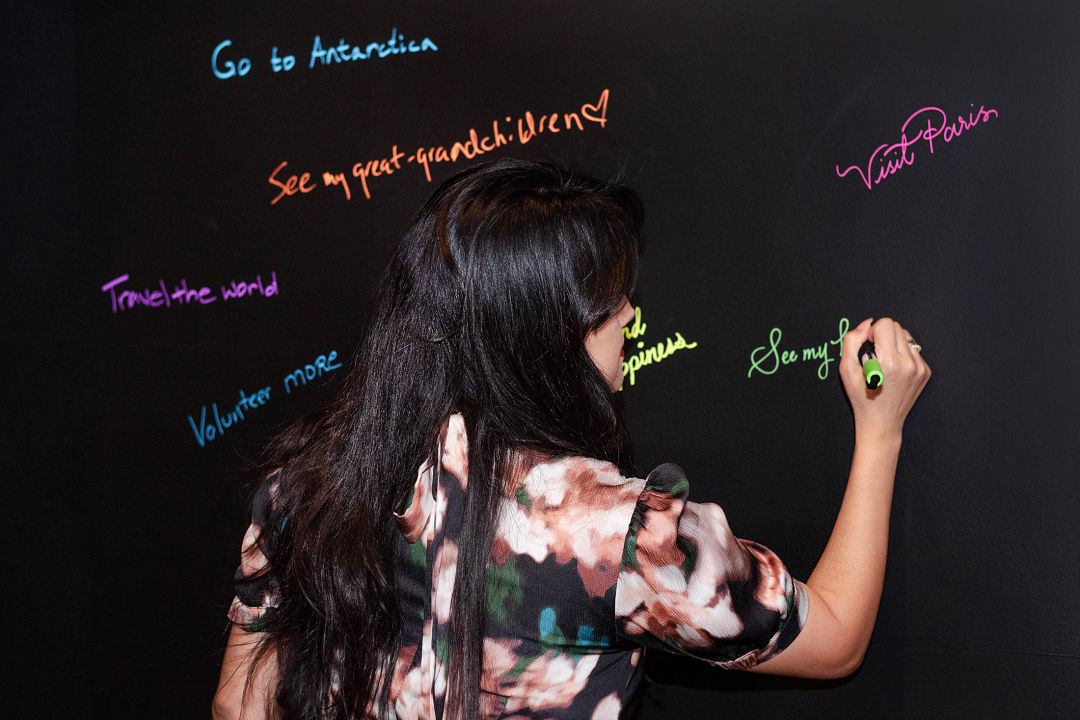 A person writing in neon ink on a black wall.