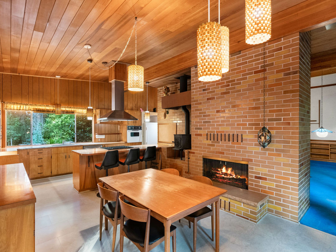 Kitchen with wood paneled cabinets, ceiling, and walls, plus wooden dining table and chairs, and brick wall with fireplace