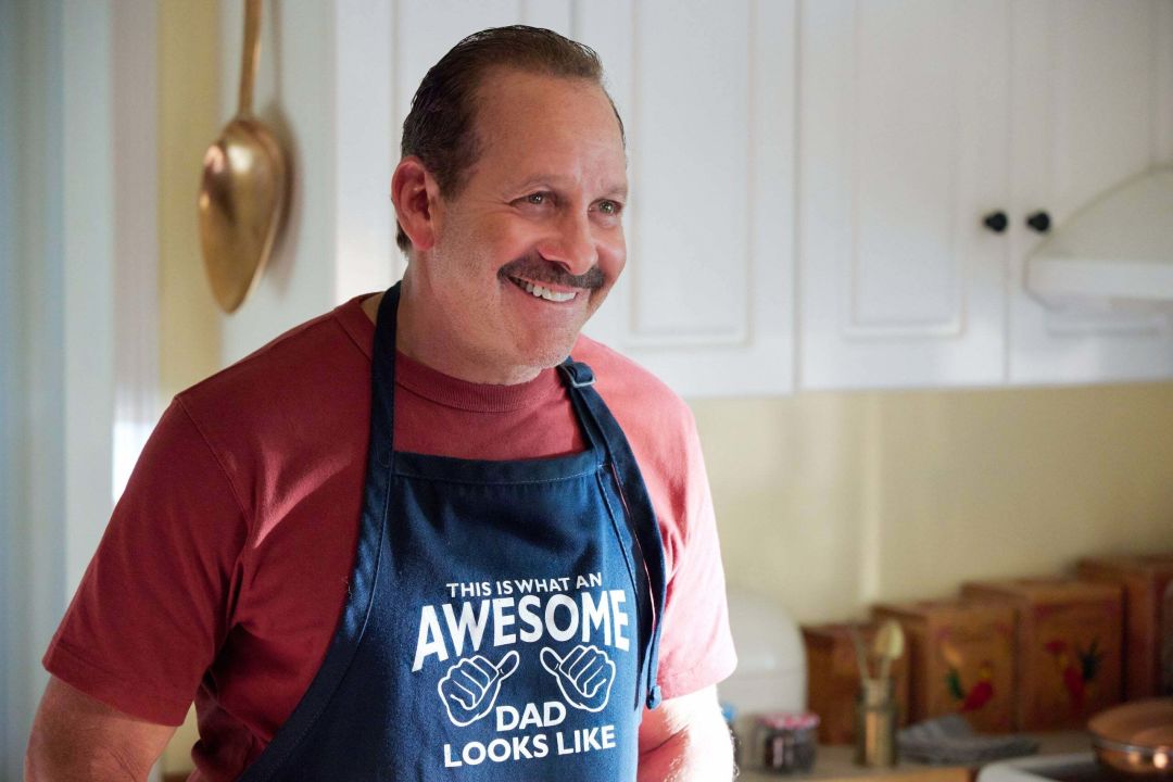 Smiling man with a mustache wearing an apron that says This is what an awesome dad looks like, with a drawing of hands with the thumbs pointing at the wearer