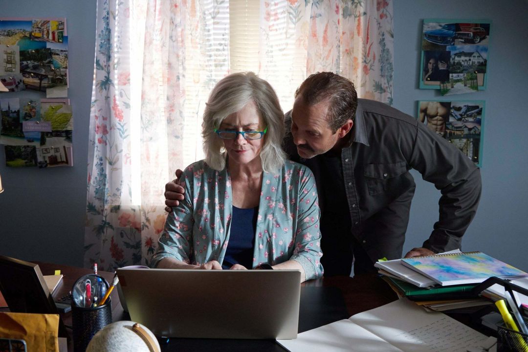 A woman sitting at a desk working on a laptop, and a man with his arm around her looking on