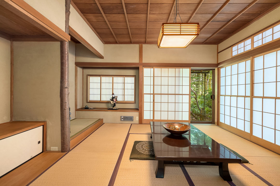The interior of a tea house. There's a low table in the middle of the room, two large alcoves to the left, and sliding wood-and-paper screens ahead and on the right wall.
