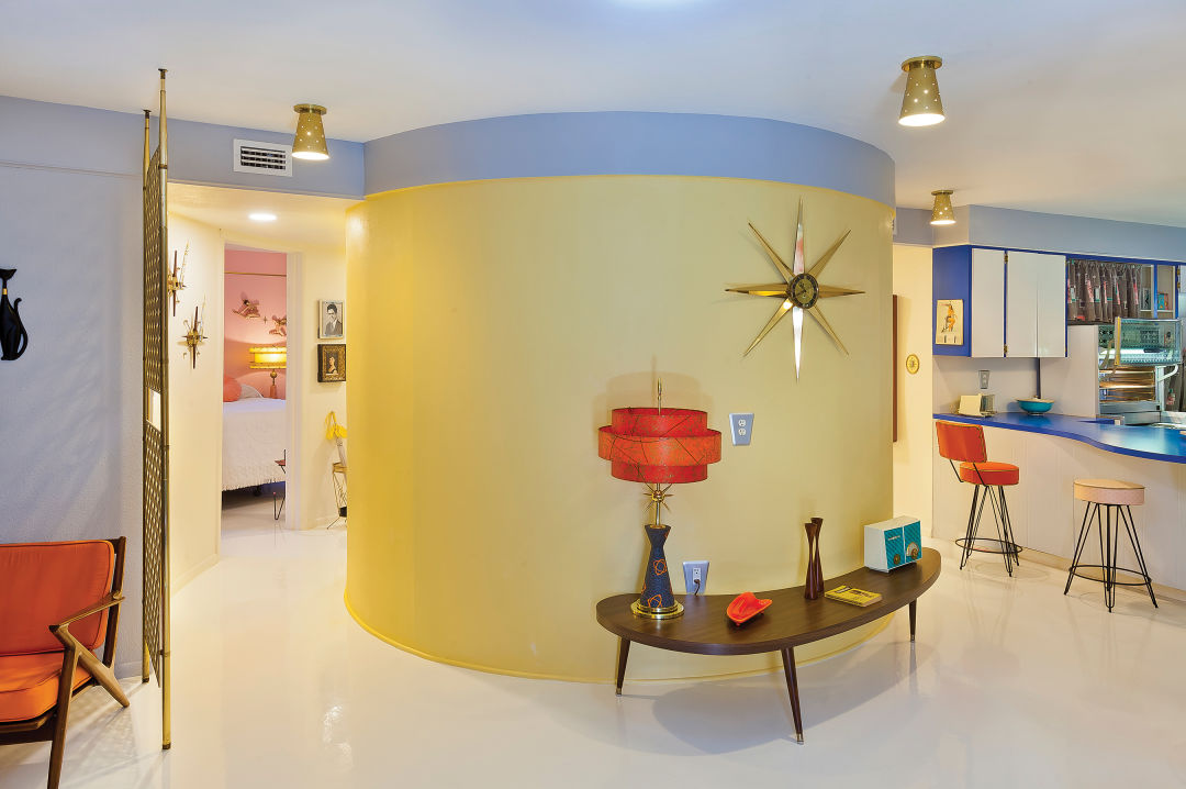 A round, single bathroom with a circle bathtub, curved mirror and a rounded sink and countertop sit at the center of the living space.