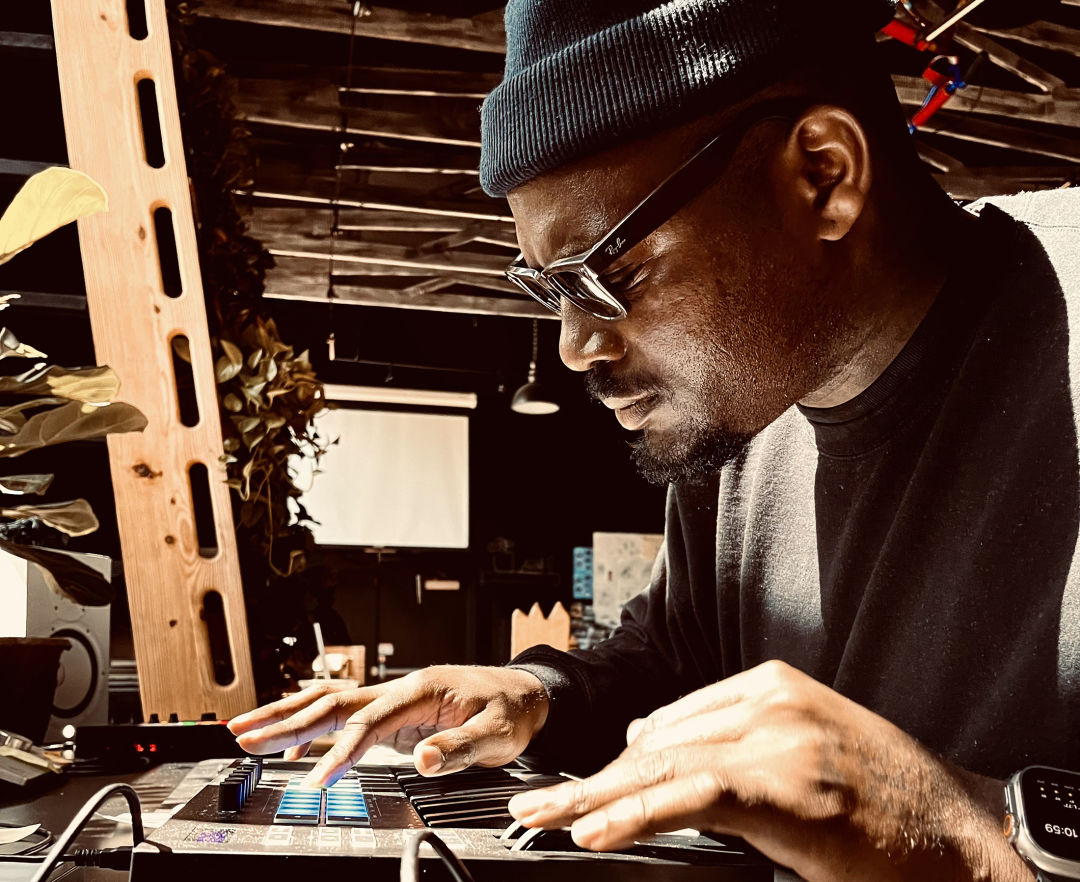 A man in a beanie sits closely at a computer and types.