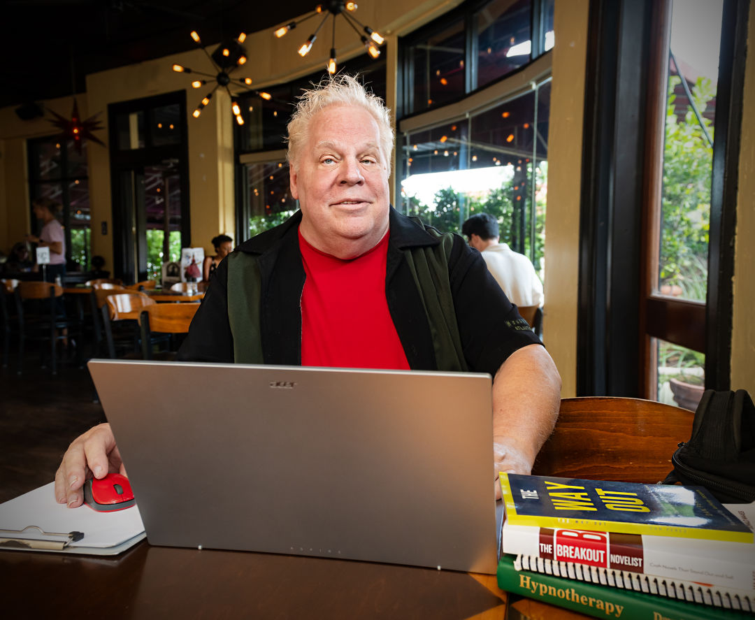 A masculine-presenting person on a laptop at a café, with books on hypnotism.