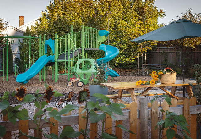 A blue and green play structure with a rounded-picket fence in the foreground