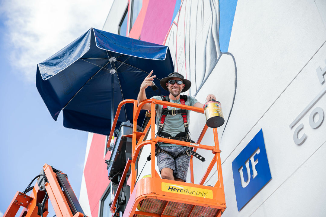 Local artist Matt McAllister on a lift, painting baseball icon "Buck" O'Neil in the Rosemary District.