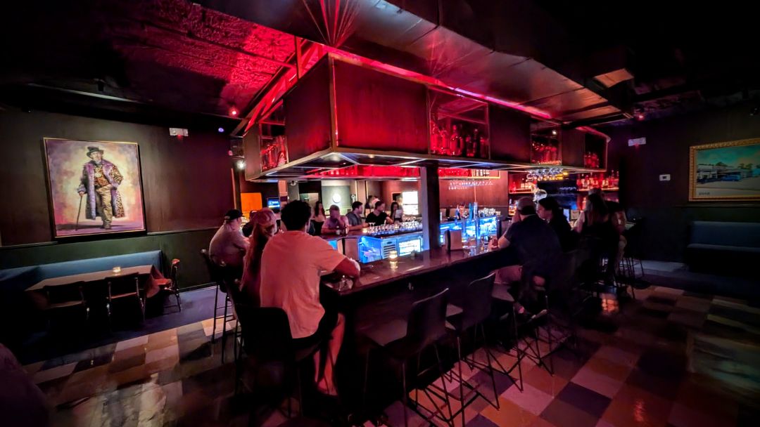 Interior of a dark bar with lights over the bar area and people sitting around it