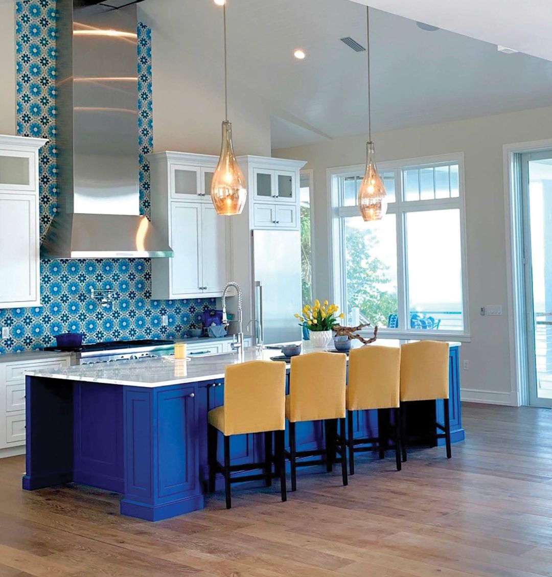 This vibrant blue kitchen island anchors the room, while a vintage-style backsplash travels up the wall. Yellow stools, pendants and fresh tulips pop against them.