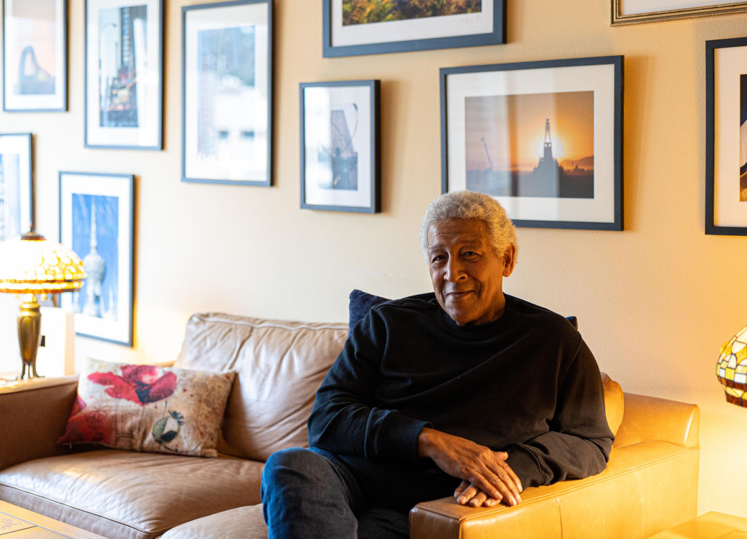 Sergio Ortiz sits on his couch in front of a wall of framed photos