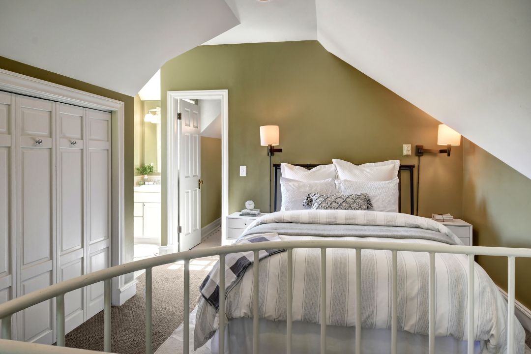 A bedroom with green walls and white trim. A full bed is under a sloping ceiling to the right, and set of built-ins is on the wall to the left.