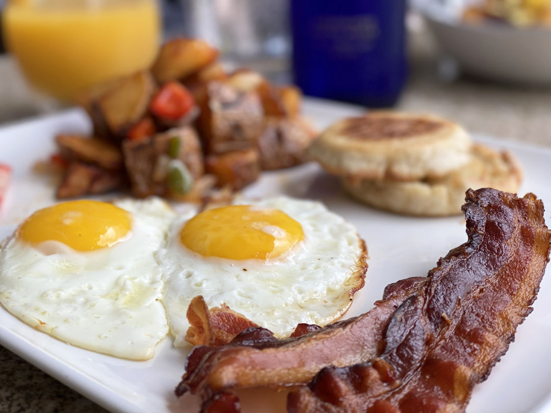 Breakfast plate of sunny side-up eggs, bacon, English muffin, and fried potatoes