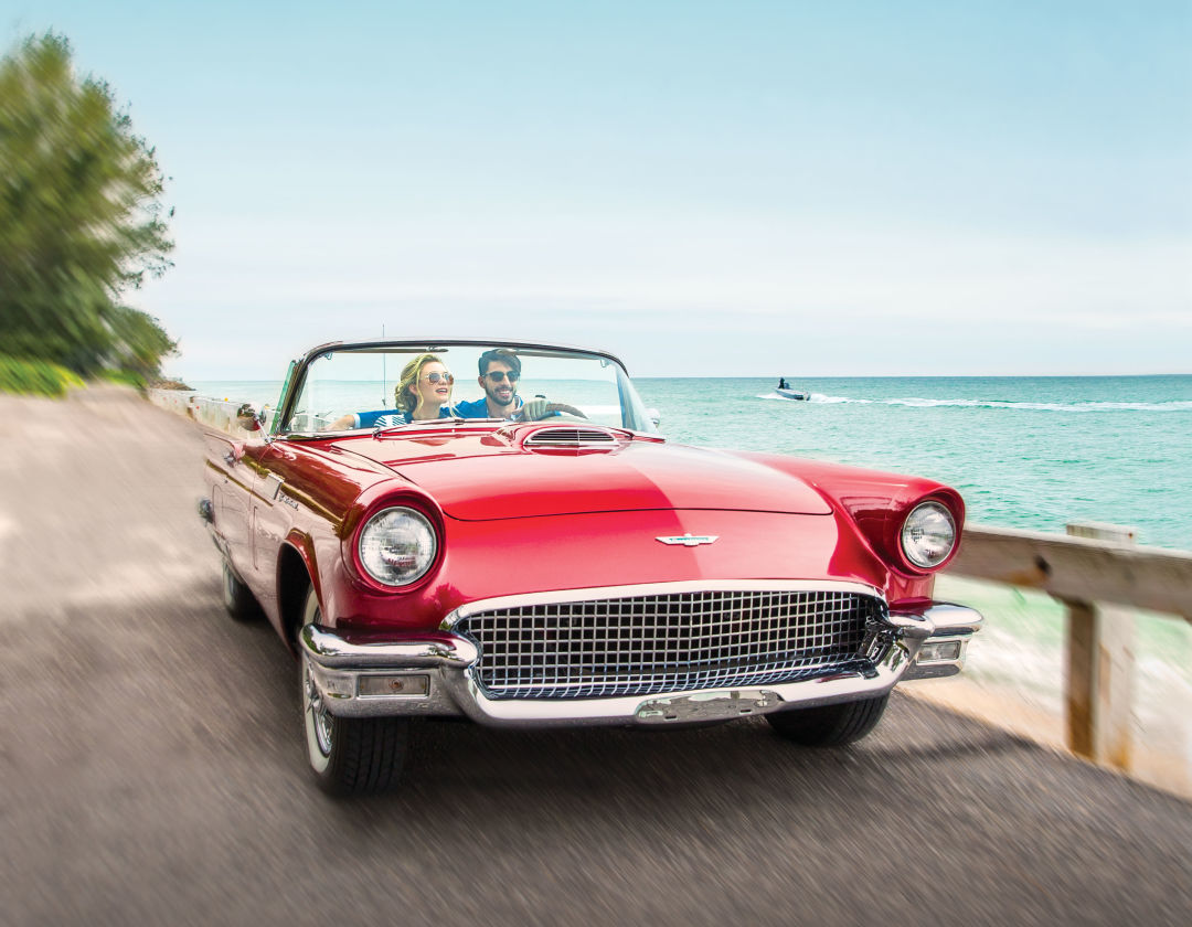 Two people sitting in red car by the beach