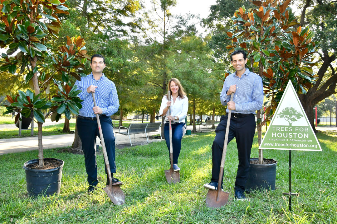 Three people stand with shovels to plant trees.