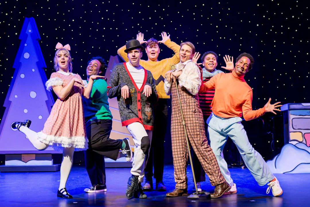 A group of actors dressed as characters from Peanuts sing and dance on stage together as a group.