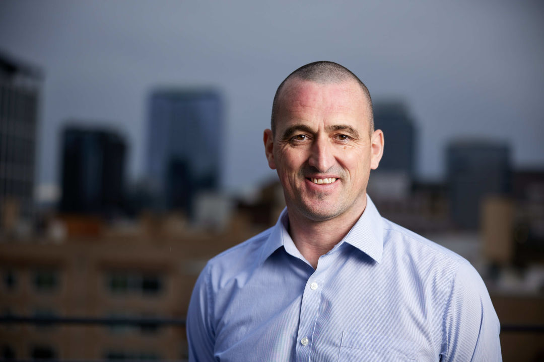A man wearing a button-up shirt and smiling in front out an out of focus city skyline