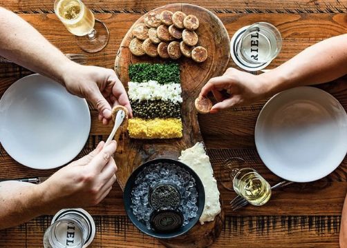 Two hands put caviar onto crackers in a spread from Riel.