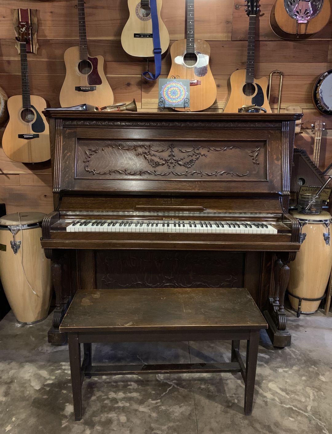 an old piano in front of a wall with acoustic guitars hanging on it