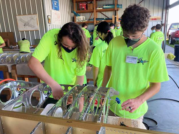 Connor Vice and Paul Moyers work on the electronics on a wing of an airplane.