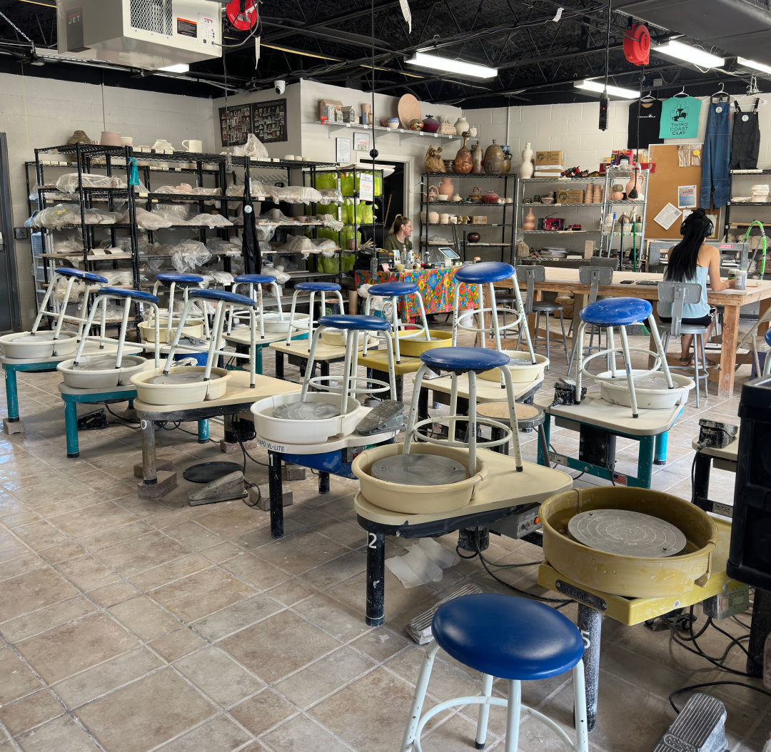 Stools placed on chairs at a pottery studio. There are also empty throwing wheels.
