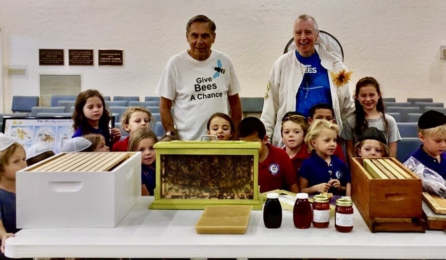 Picture of two beekeepers from suncoast beekeepers association showing a group of children a demonstration hive