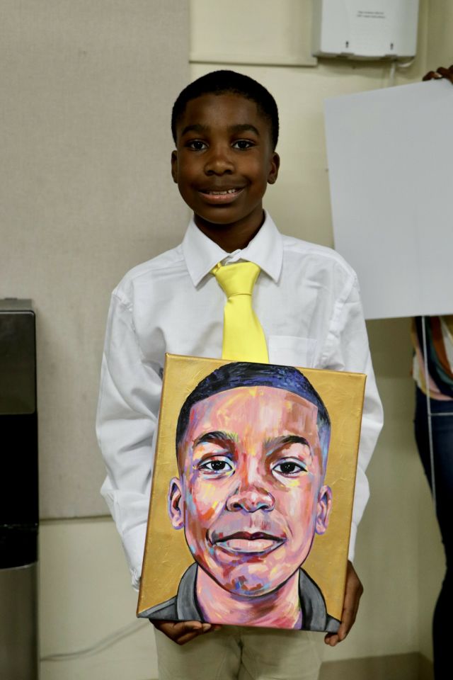 A 12-year-old student holding a portrait his art teacher painted of him on graduation day from elementary school.