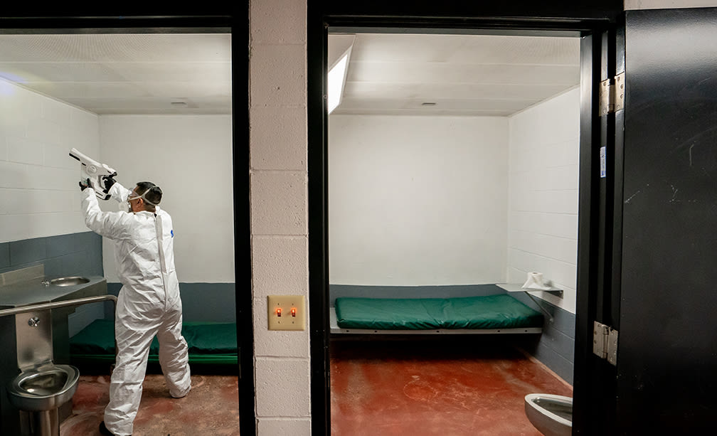 Man in a white protective suit shines UV light on the wall of a jail cell.