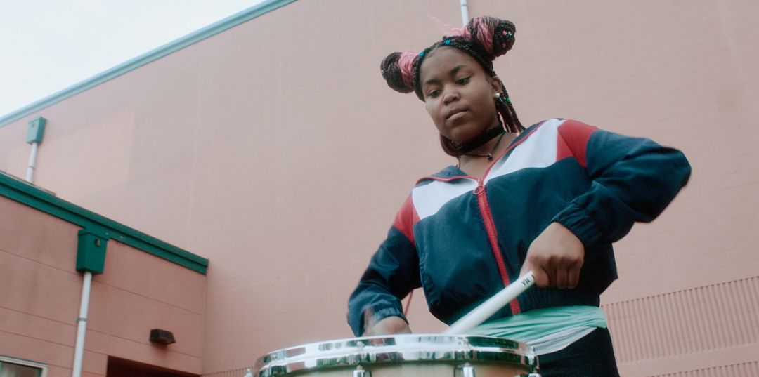 A girl in a blue jacket plays the drum.