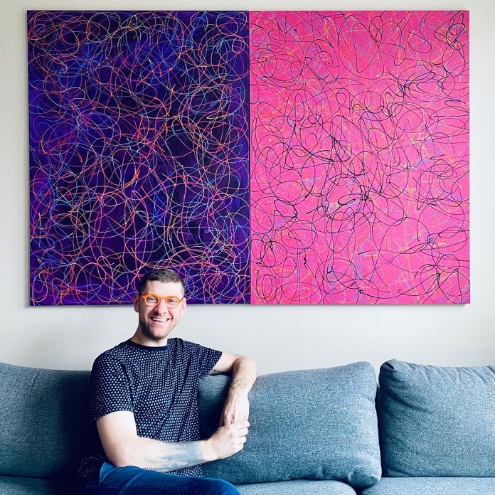 Zac Cooper sits on a couch in front of a large canvas painting
