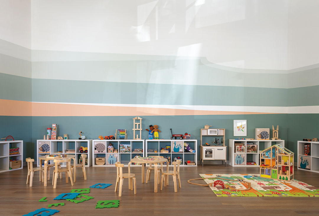 a room with low chairs, tables, and shelves, plus a play kitchen and letter tiles on the floor
