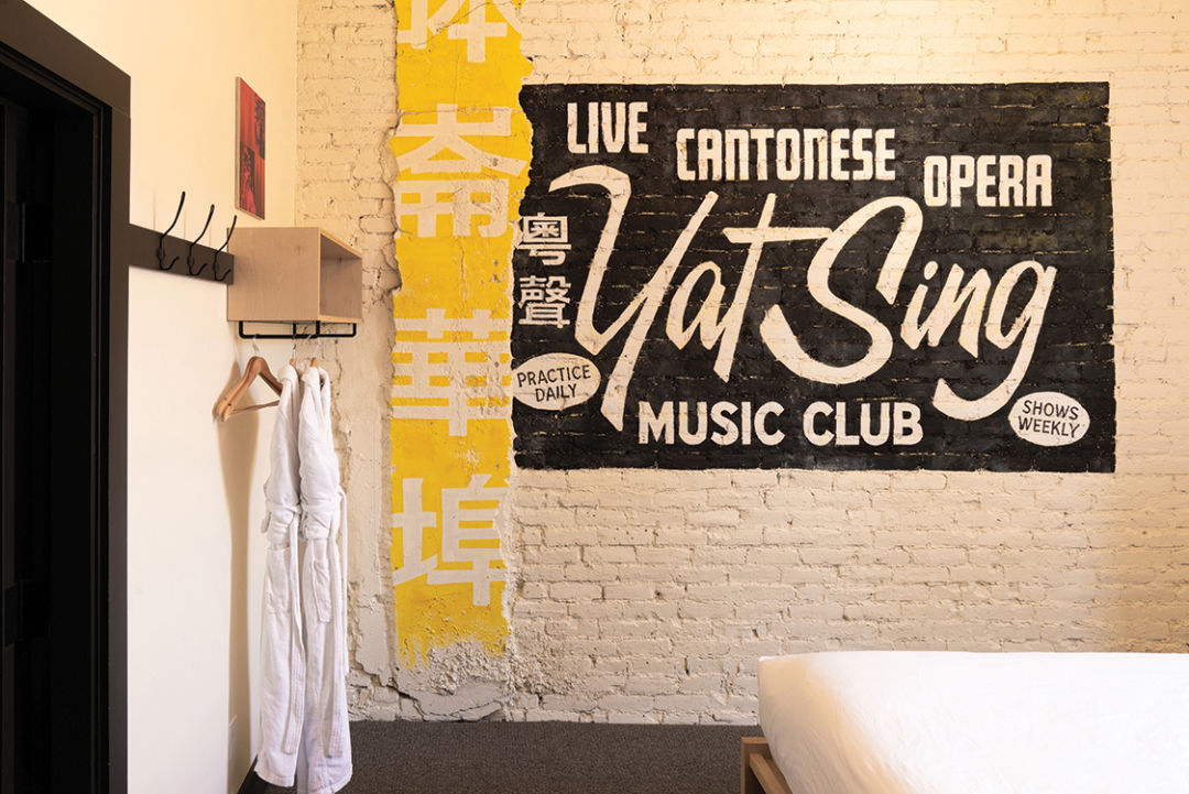 A brick wall in a hotel room with an old-looking sign painted on it for "Live Cantonese Opera: Yat Sing Music Club"