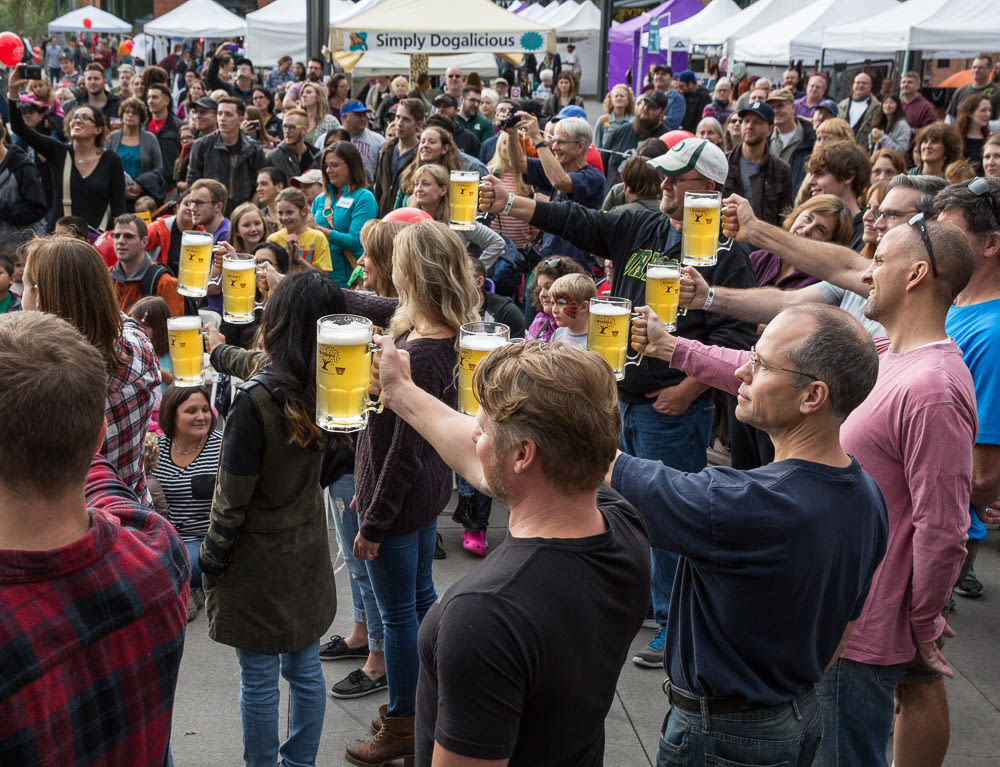 People in a crowd, some with a full glass beer stein at the end of their outstretch arm