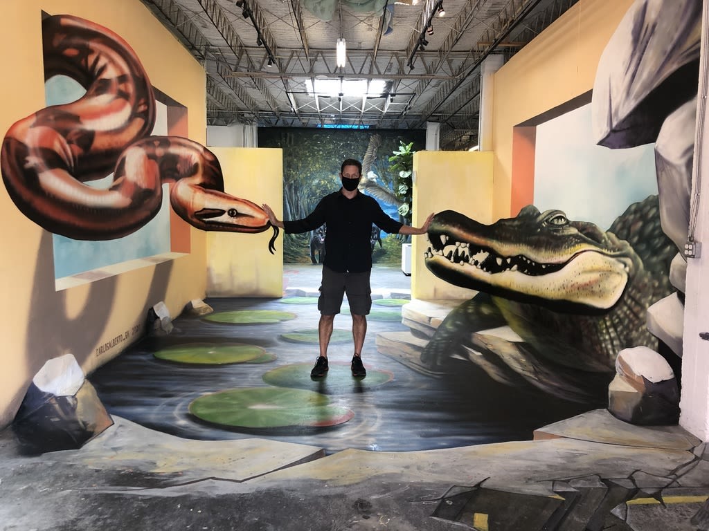 Man stands on 3D animal illusion chalk painting.