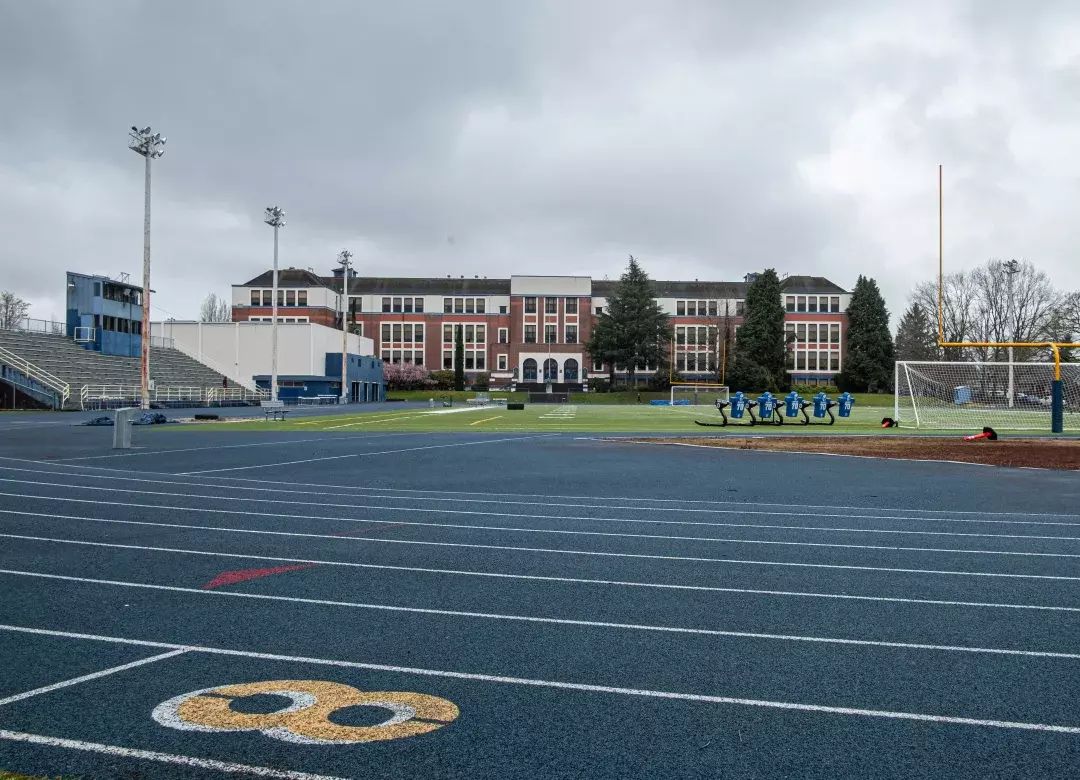 A brick school building in the distance, with an athletic field and track in the foreground