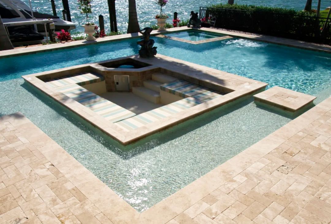 A Freestyle Pool & Spa custom pool with a sun shelf surrounded by a travertine deck area.