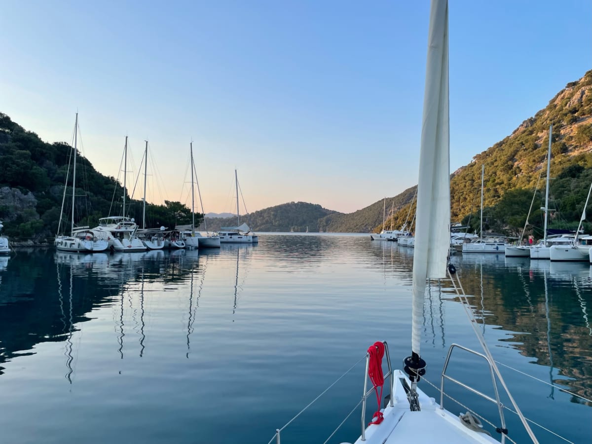 Sailboat sailing through coastal hills under bright sun.
